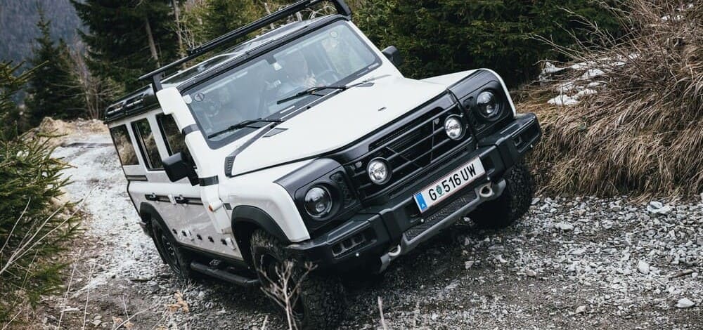 El Ineos Grenadier en color blanco en una carretera de montaña visto desde la parte delantera y lateral derecha