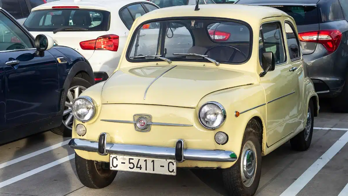 Seat 600 clásico con matrícula española antigua aparcado entre coches modernos