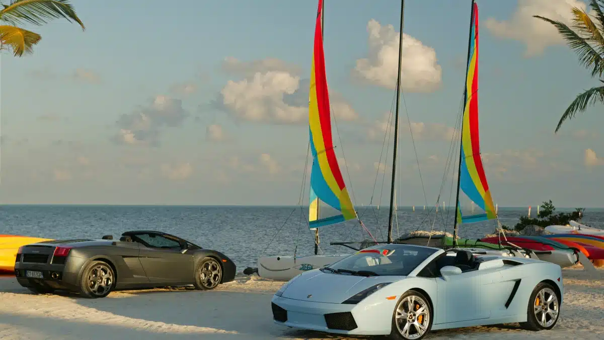 Dos Lamborghini Gallardo Spyder aparcados frente a una playa con veleros al fondo