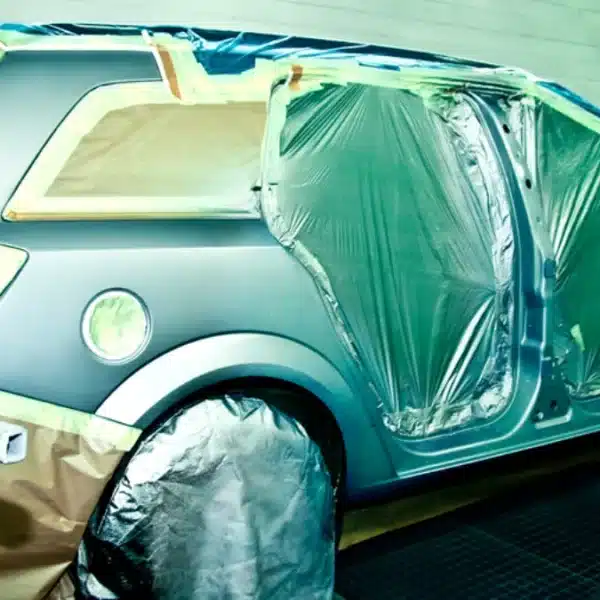 Coche enmascarado con plástico siendo pintado en un taller de chapa y pintura