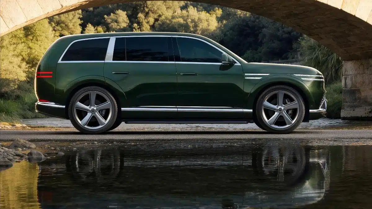Genesis GV90 visto de perfil en color verde oscuro bajo un puente de piedra, con reflejo en el agua