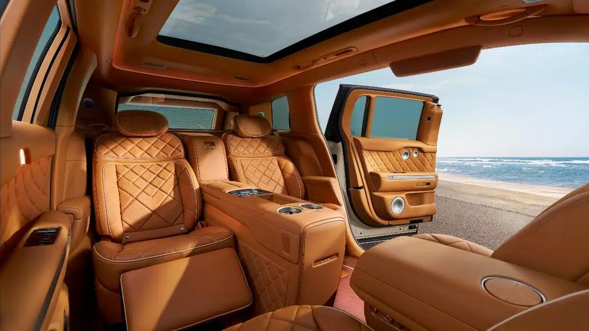 Interior trasero del Genesis GV90 Neolun con los asientos ejecutivos individuales en cuero cognac y puerta abierta hacia la playa