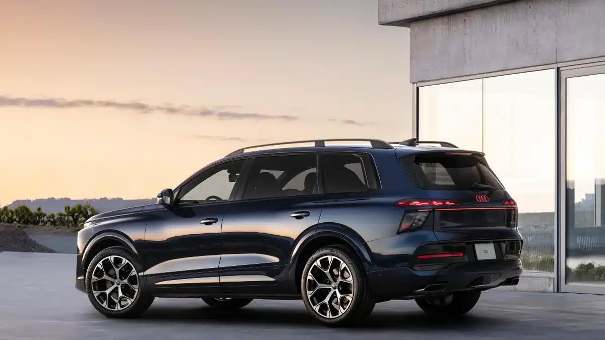 Audi Q9 visto de perfil trasero junto a una vivienda de diseño al atardecer