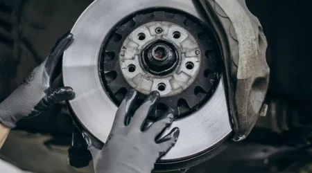 Mecánico sujetando la pinza de freno mientras revisa el disco de freno de un coche elevado en el taller