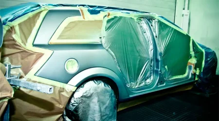 Coche enmascarado con plástico siendo pintado en un taller de chapa y pintura